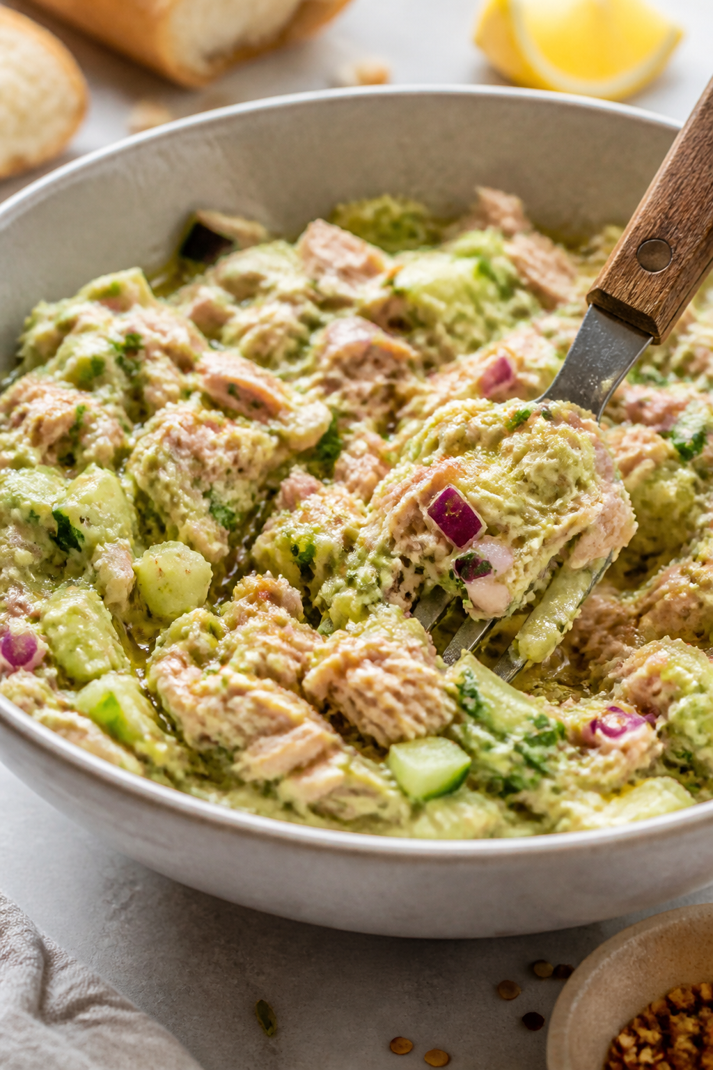 Close-up detail: Creamy avocado tuna salad mid-prep in a ceramic mixing bowl, fork gently folding fl