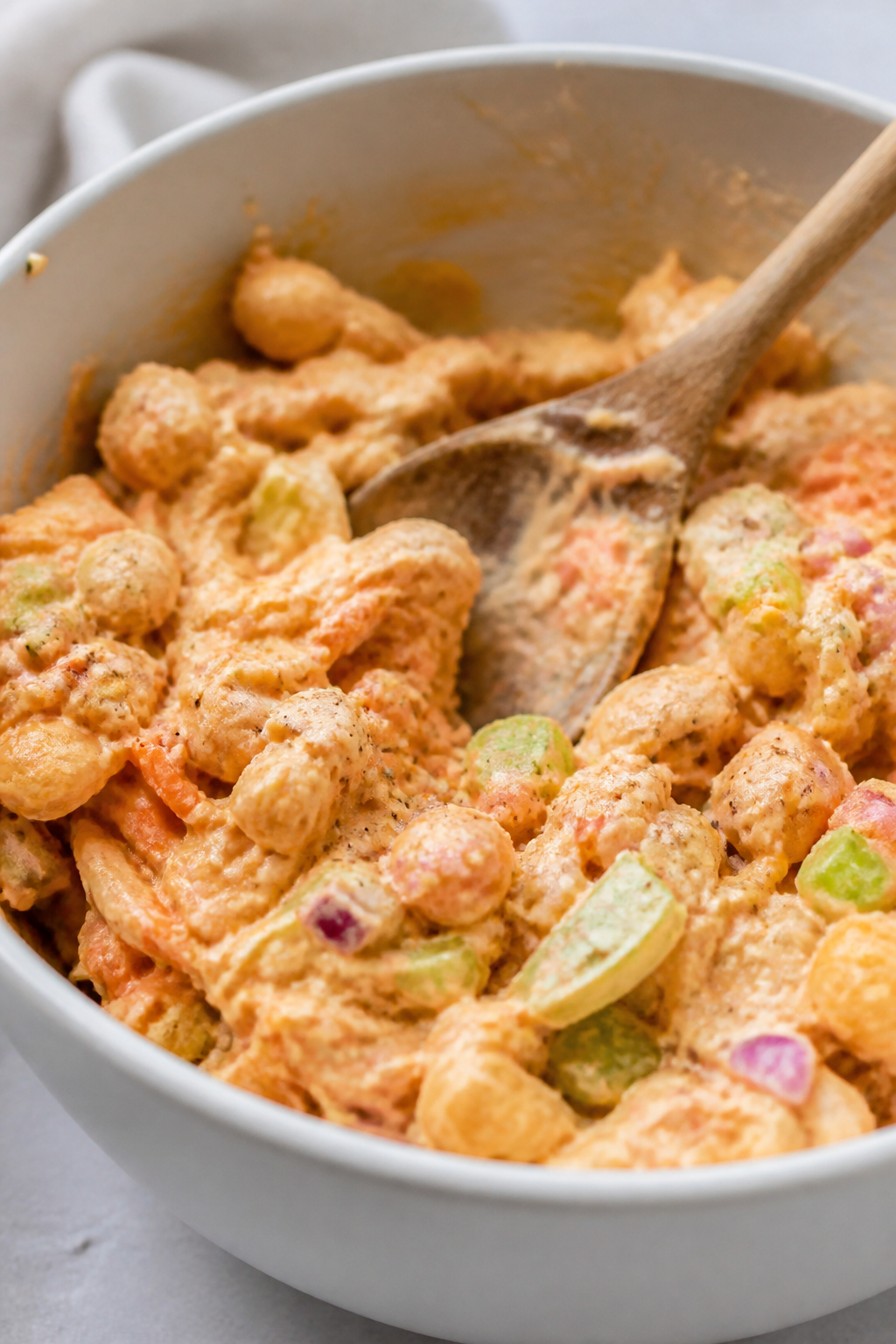 Close-up detail: Creamy buffalo ranch chickpea chicken salad being mixed in a matte white bowl, show