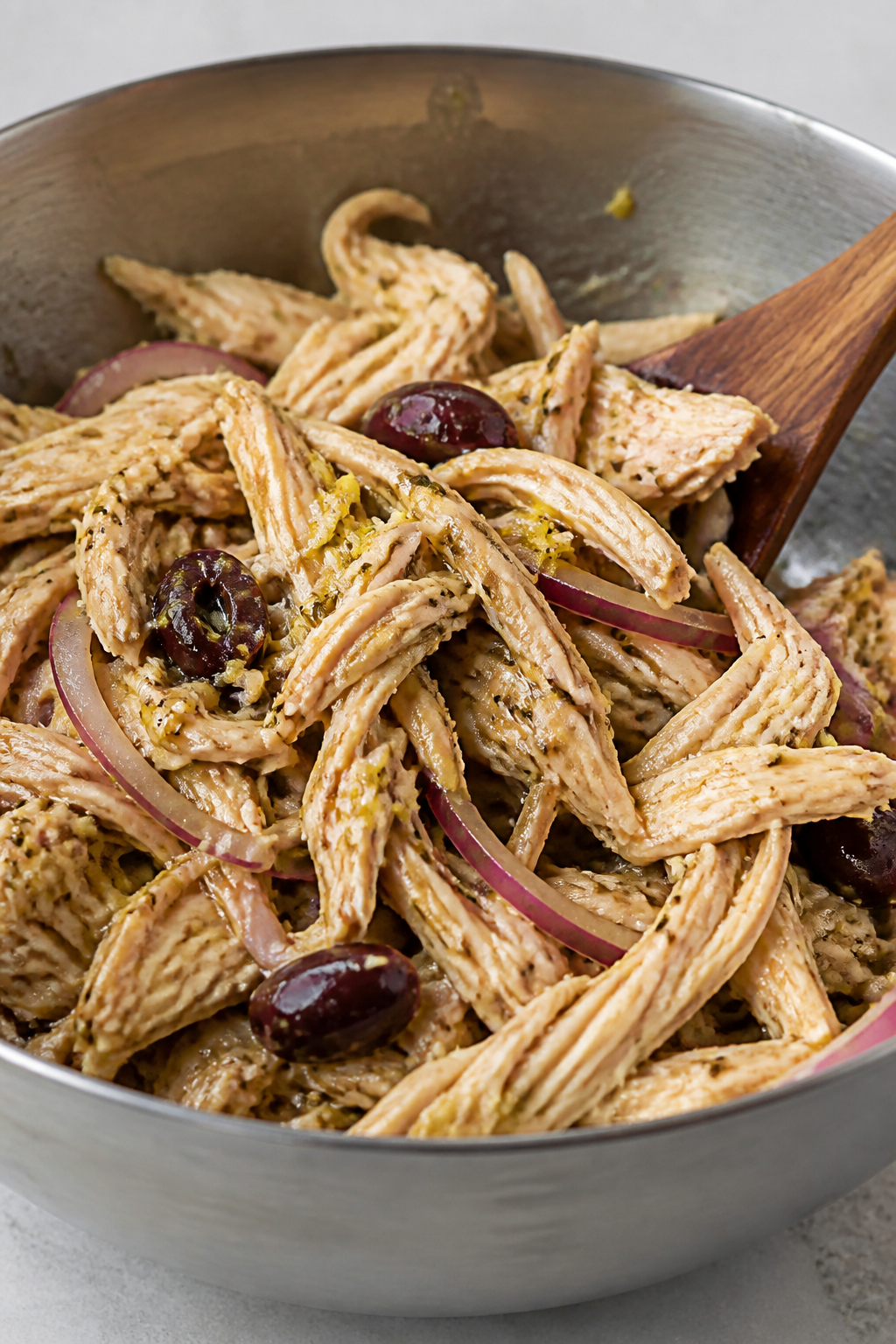 Cooking process close-up: Juicy shredded rotisserie chicken being tossed with a glossy Greek dressin