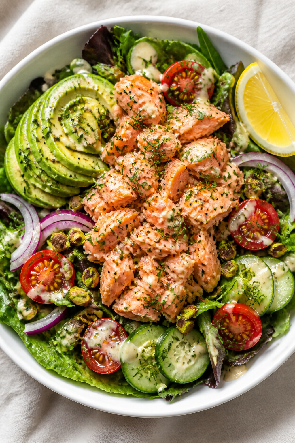 Overhead shot of Lemon Garlic Salmon Salad Bowl fully assembled: bed of mixed greens lightly glossed