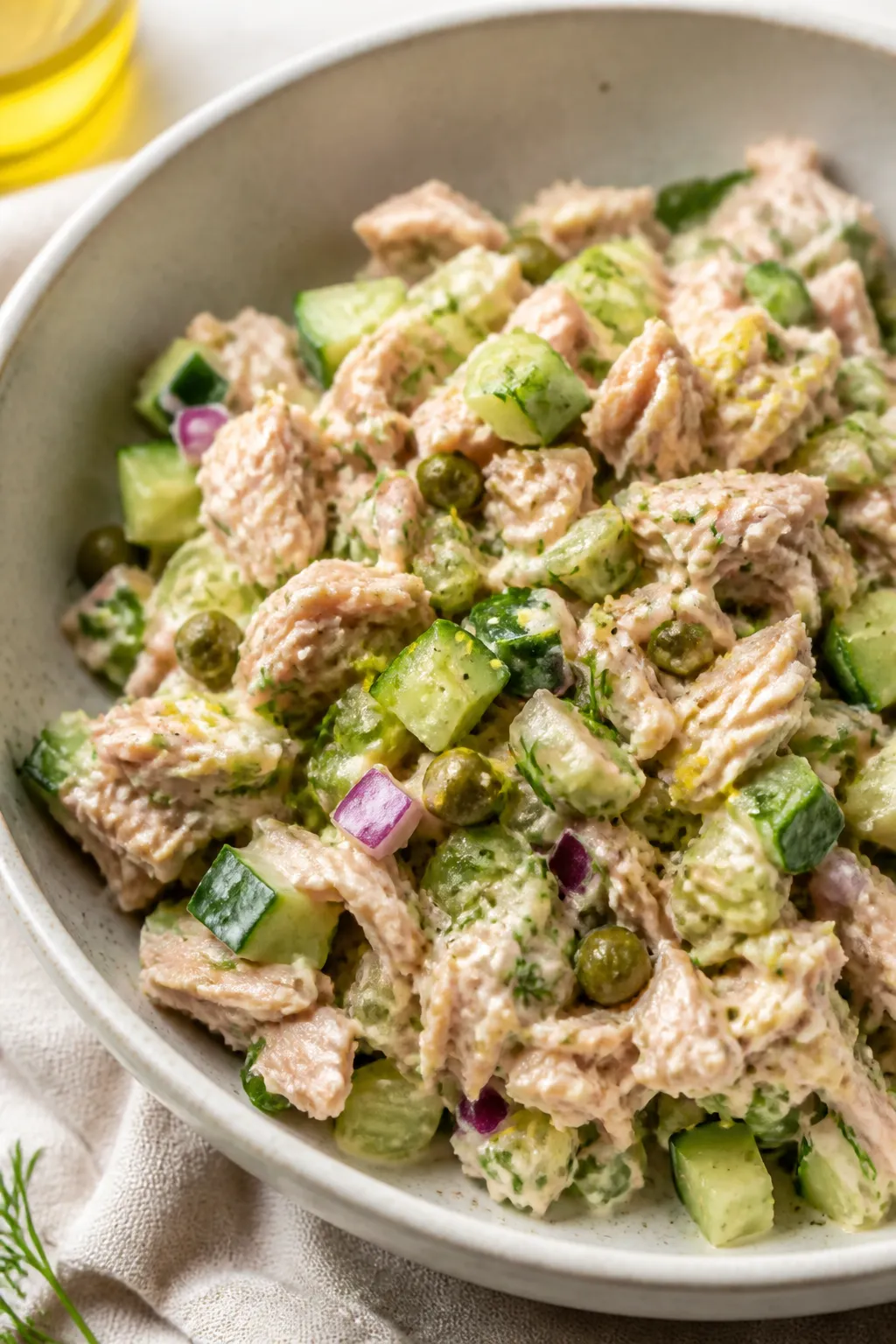 Close-up detail: A bowl of prepared tuna cucumber salad just after mixing, showing glossy chunks of