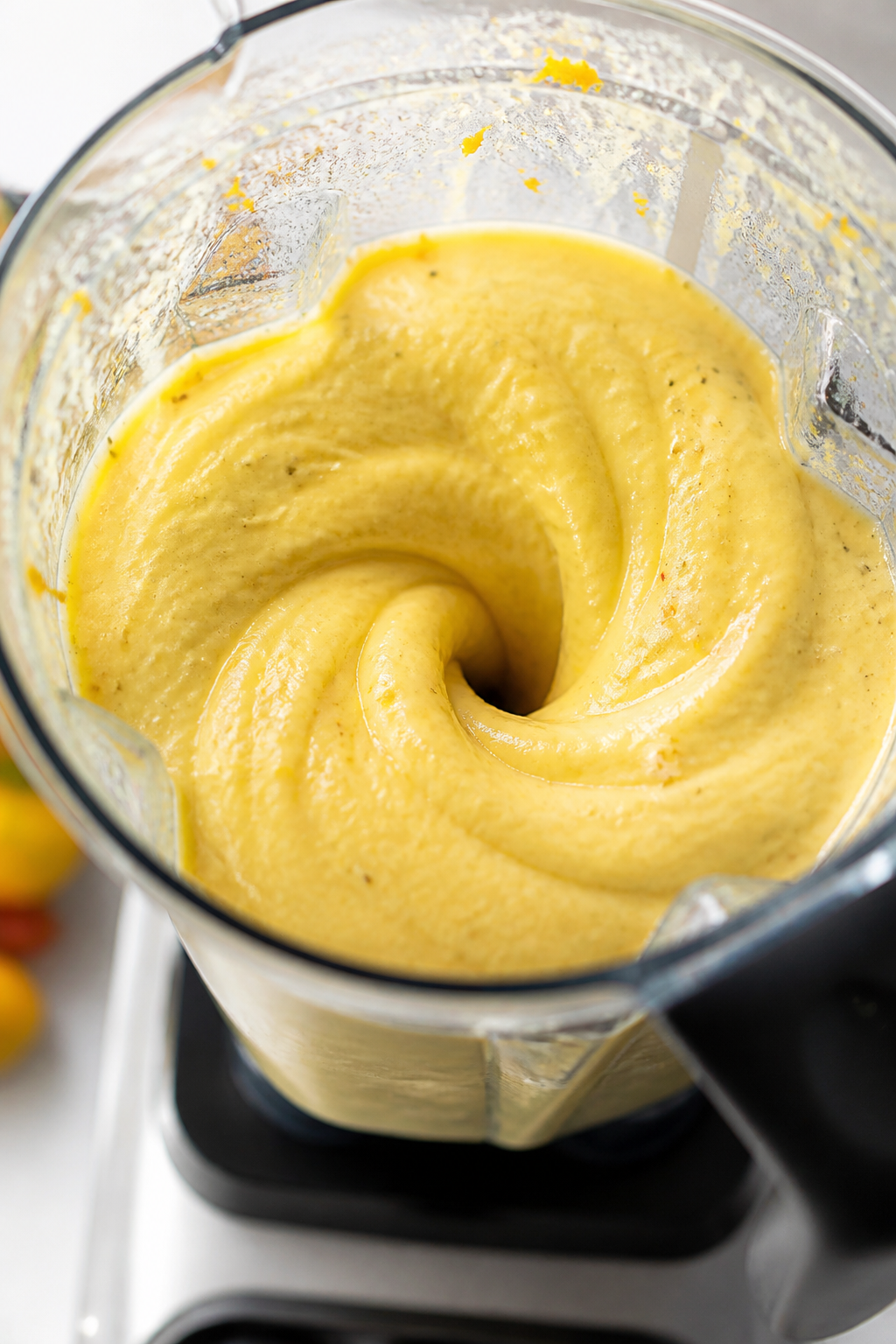 Close-up detail: Thick, silky mango peach protein shake mid-blend in a clear high-speed blender, cre