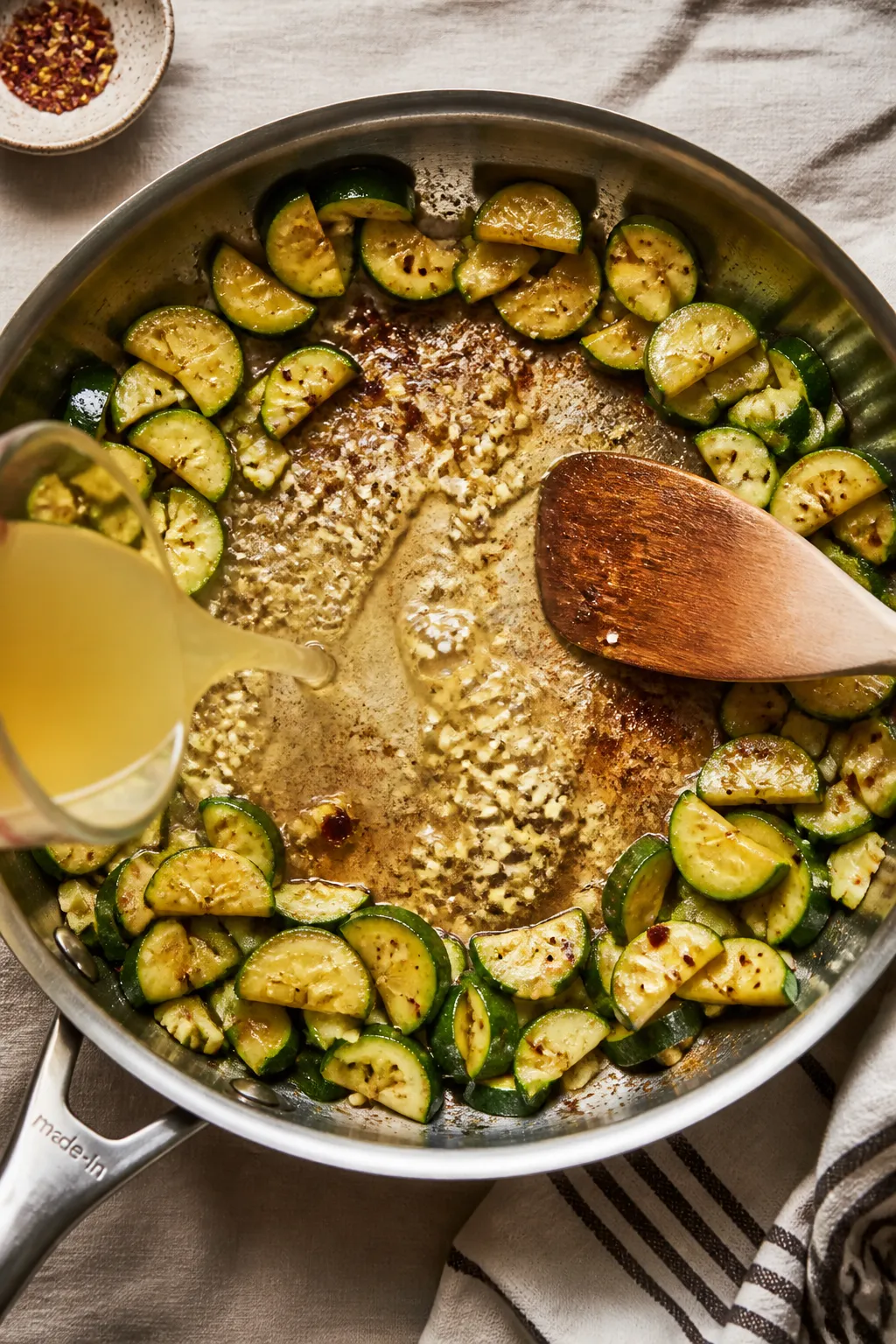 Cooking process action: Overhead shot of the zucchini pushed to the skillet’s edges while butter m