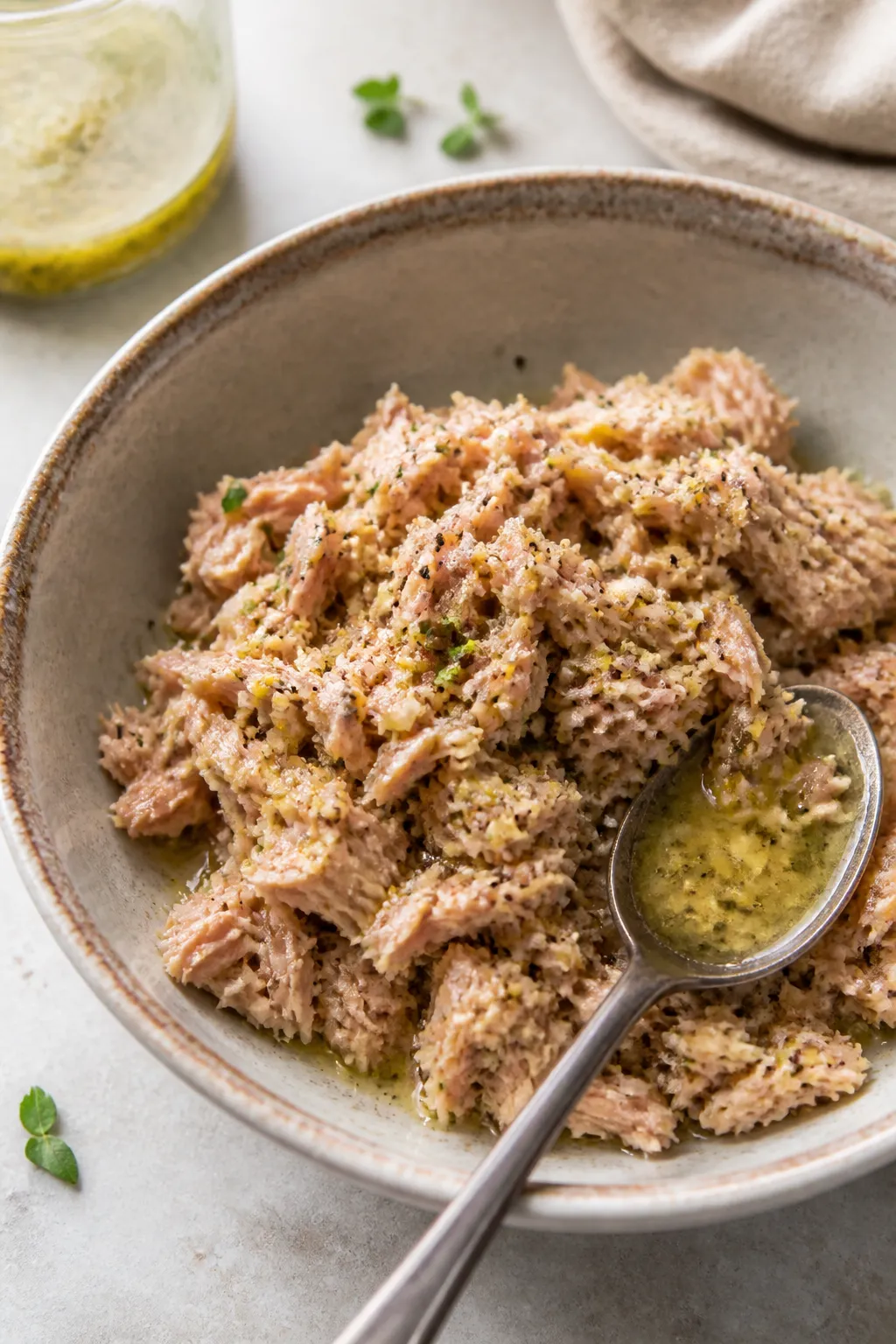 Cooking process — tuna being seasoned: Close-up of flaked, drained tuna in a ceramic bowl tossed w