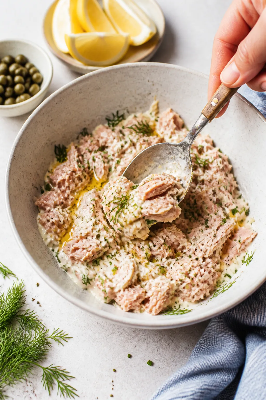 Cooking process: Tuna mix being folded gently in a ceramic bowl—visible flakes of drained tuna com