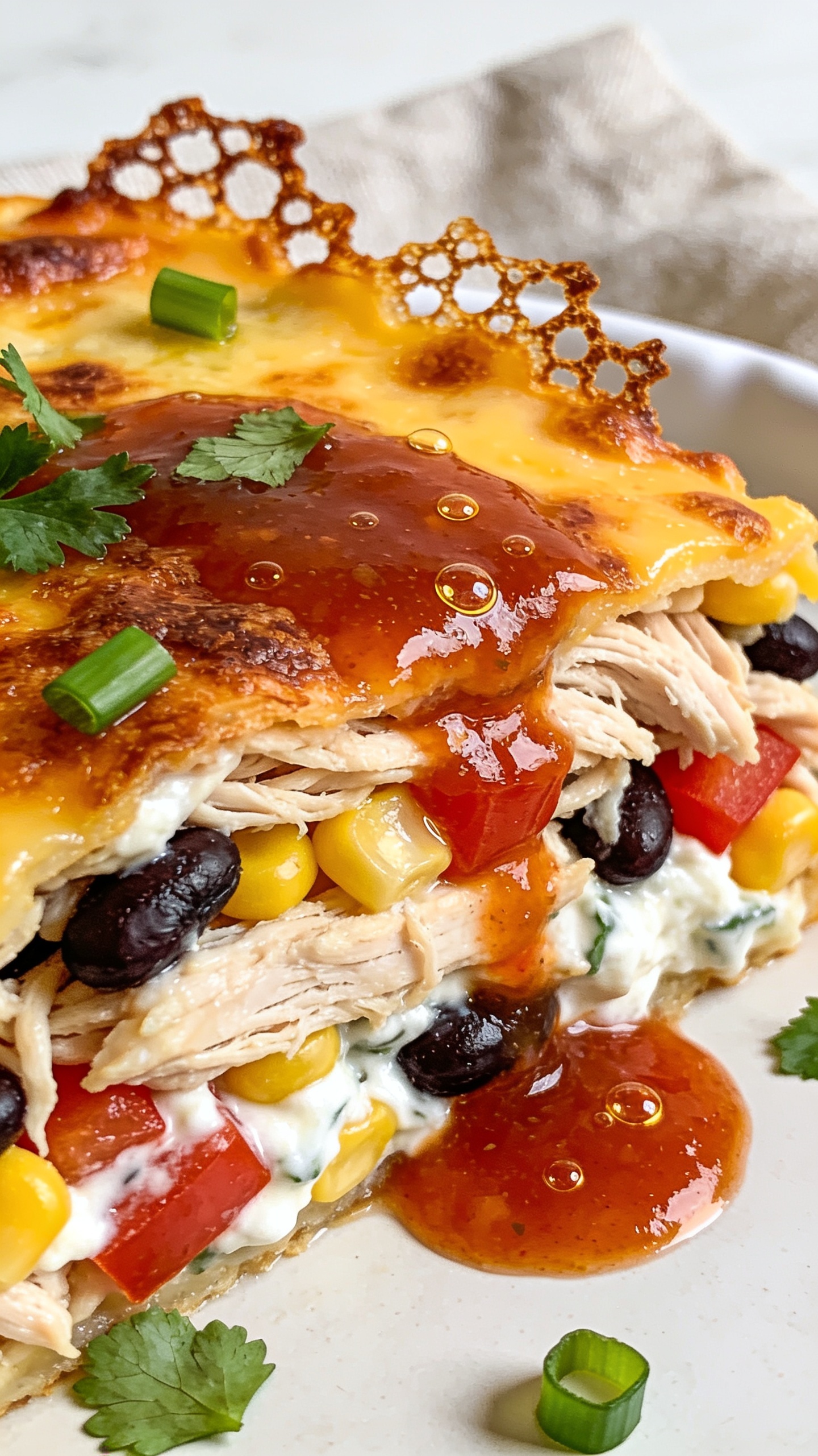 Extreme close-up from a 45-degree angle of a corner piece scooped from the same baking dish, filling 90–95% of the frame. Focus on the layered interior: moist shredded chicken, black beans, sweet corn, diced red bell pepper, and a creamy Greek-yogurt-cottage-cheese mixture binding everything, all beneath a bronzed, bubbly cheddar–Monterey Jack top with crisp, lacy edges. A light drizzle of glossy salsa roja pooled along the top, with micro-beads of oil catching the light. Fresh cilantro and green onion scattered sparingly. Bright natural light raking across the surface, shallow depth of field, background softly blurred neutral napkin and edge of the white dish, rich textures and irresistible sheen.
