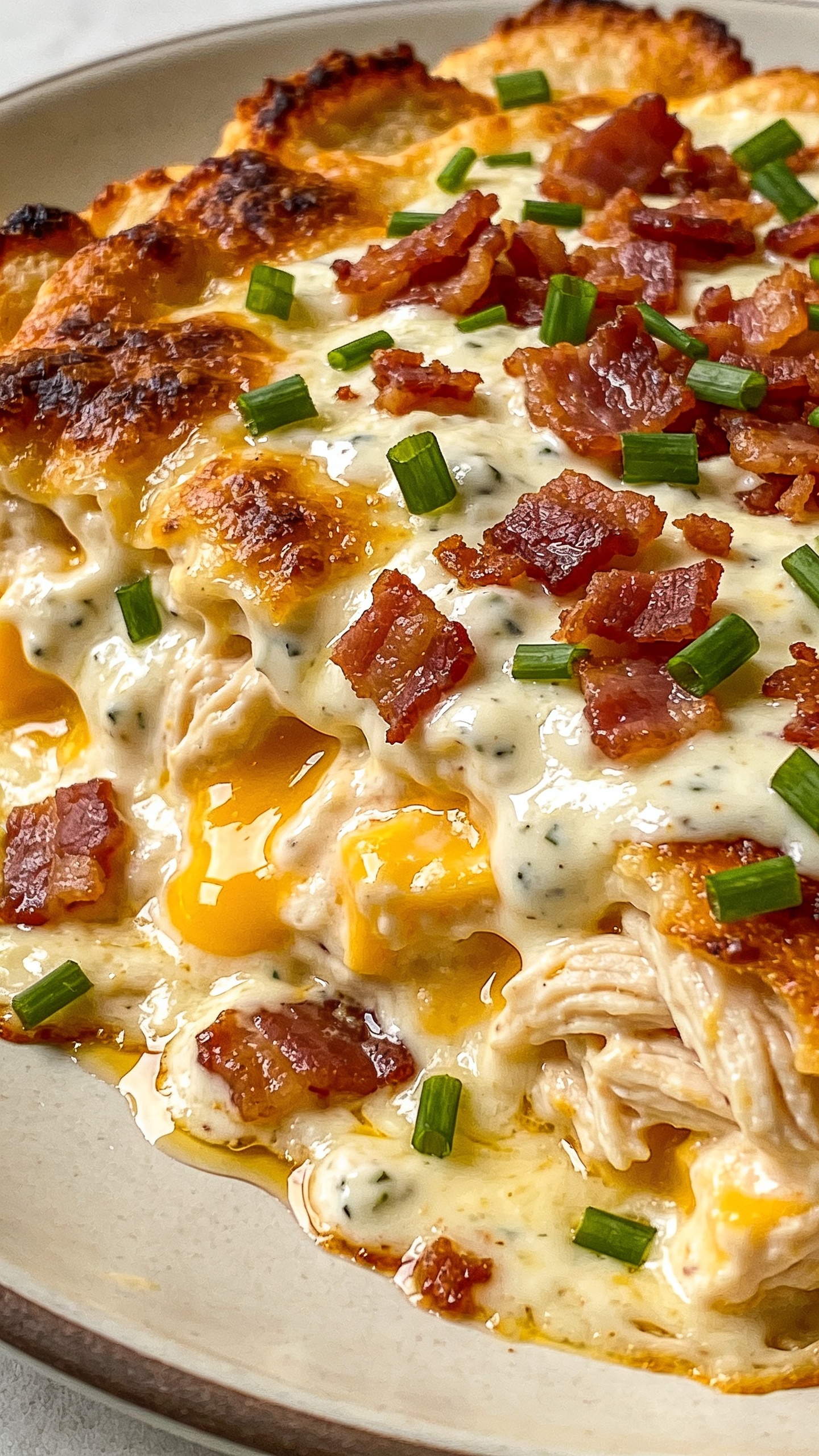 Extreme close-up angled shot focusing on textures: the surface of the Air Fryer Crack Chicken showing crispy browned edges, creamy ranch-cheese layer bubbling and glossy, pockets of cheddar melt, generous bacon crumble, and fresh green chives scattered on top. A light sheen of rendered bacon fat mingles with the melted cheese around the chickenâs edges. Neutral plate barely visible at the rim, bright natural lighting, shallow depth of field isolating the front edge of the chicken, 90â95% of frame filled with the dish, consistent styling with the other images, no hands or text.
