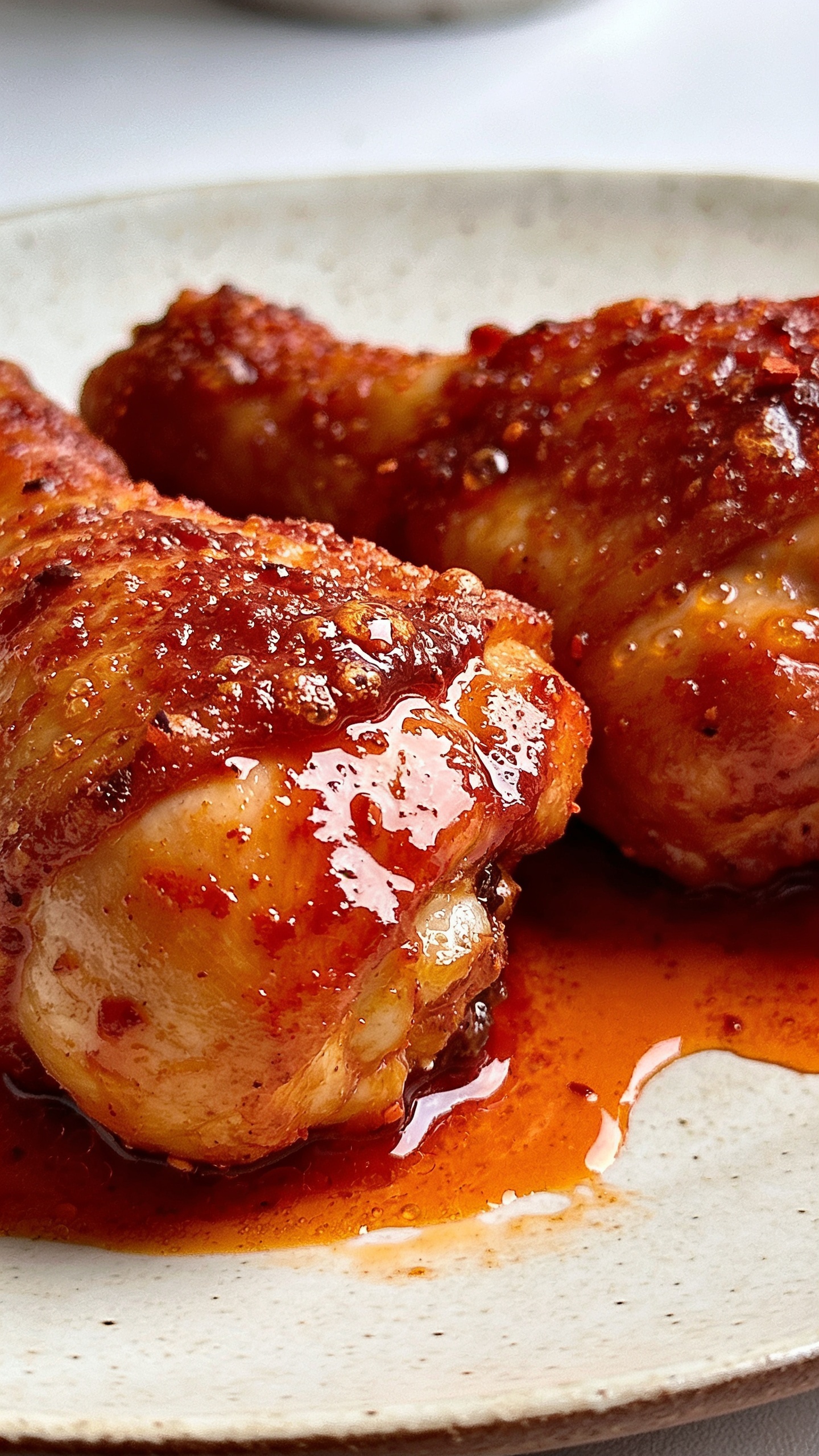 Ultra close-up hero shot of Air Fryer Nashville Hot Chicken: two golden-crisp boneless chicken thighs coated in glossy, deep-red cayenne oil glaze, stacked on thick butter-toasted white bread with visible buttery sheen, topped with crinkle-cut dill pickles; extra glaze pooling slightly around the toast edges; shatter-crisp crust texture with tiny blistered bits, micro-bubbles in the glaze; vibrant, warm color palette with fiery reds and amber highlights; bright natural side lighting, shallow depth of field, soft blurred background of a neutral ceramic plate; 90–95% frame filled with food; premium food-blog styling, no text, no hands.