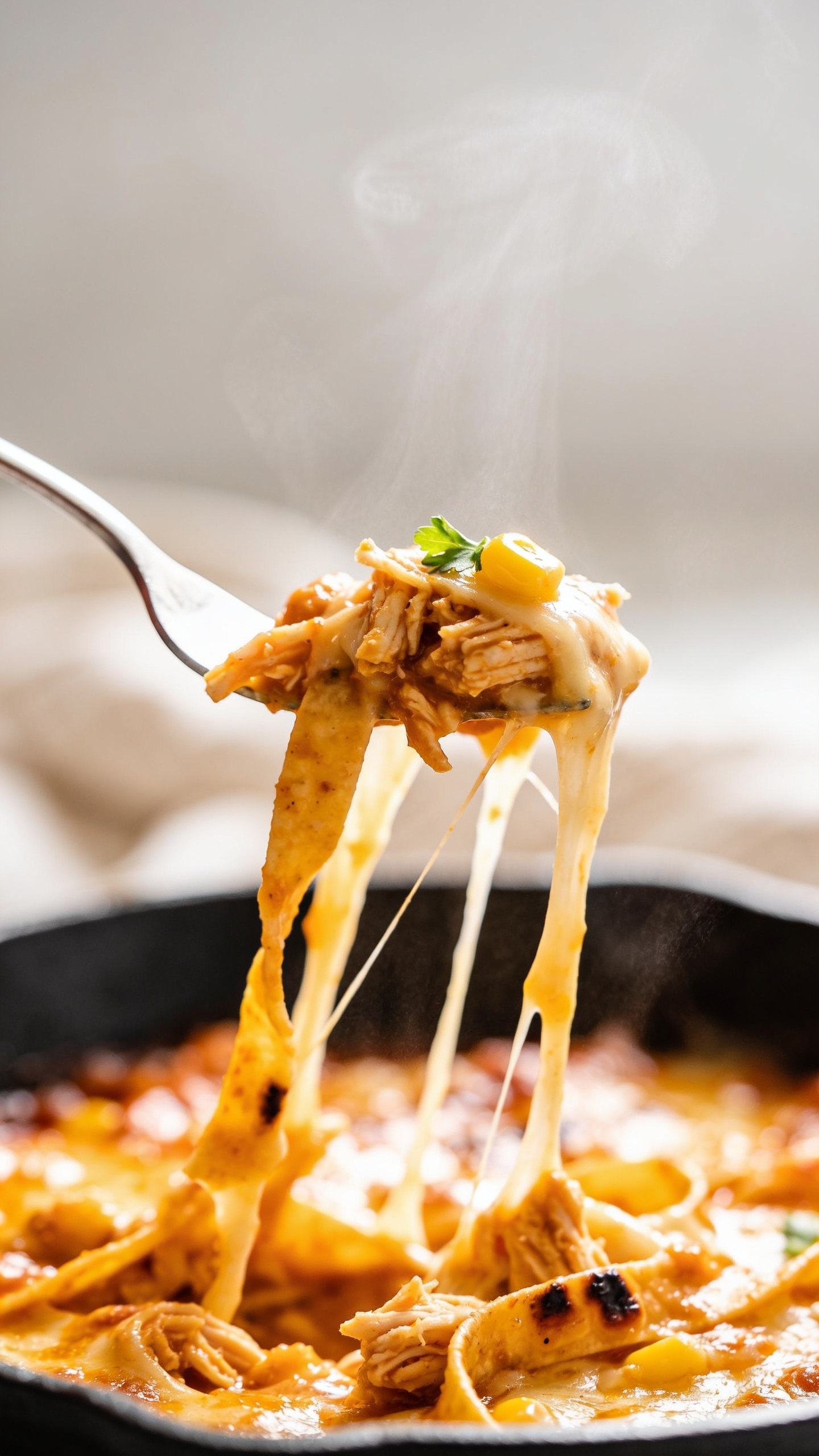 Action moment: extreme close-up of a fork lifting the perfect cheesy bite from the chicken enchilada skillet one inch above the pan, cheese stretching in long glossy ribbons back to the bubbling skillet, saucy tortilla strips clinging, bits of shredded chicken, a kernel of charred corn and a fleck of cilantro on the bite. Visible steam rising softly, bright natural side light catching the sheen of enchilada sauce and melted cheese, background blurred to creamy bokeh, 90–95% food in frame, no hands or people, only the fork tip and the lifted bite in focus, dynamic and mouthwatering.