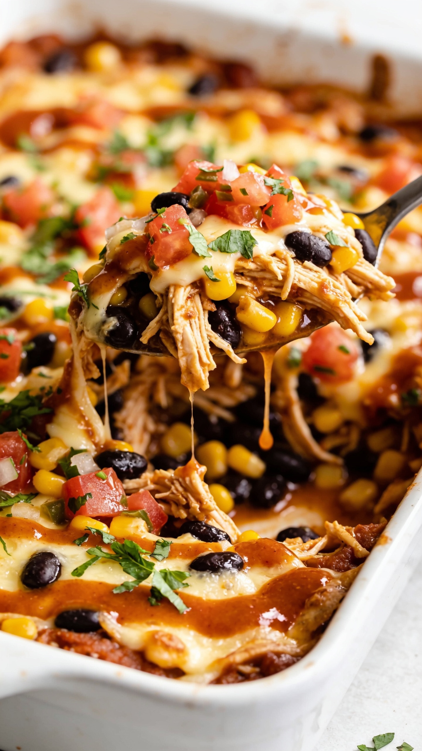 Close-up, top-down or slight 45-degree angle shot of the finished casserole showing juicy textures and toppings: shredded chicken, black beans, corn, pico, sauce, and melted cheese, fresh herbs sprinkling down, glossy sauce pooling, bright natural light, shallow depth of field, food dominating the frame (90-95%).