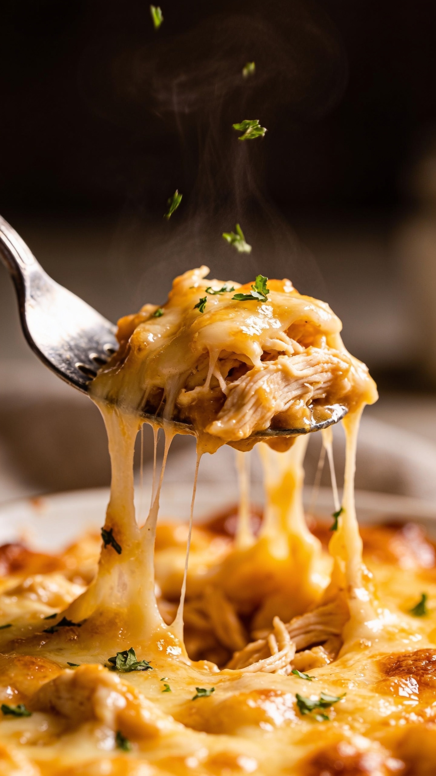 A dynamic close-up action shot: a fork lifting the perfect bite of the finished casserole, foil-cheesy strings stretching from the spoonful to the plate, glossy sauce catching the light, shredded chicken visible under the melted cheese, herbs lightly falling onto the bite, warm steam just rising, ultra-close crop, shallow depth of field, premium food-blog styling.