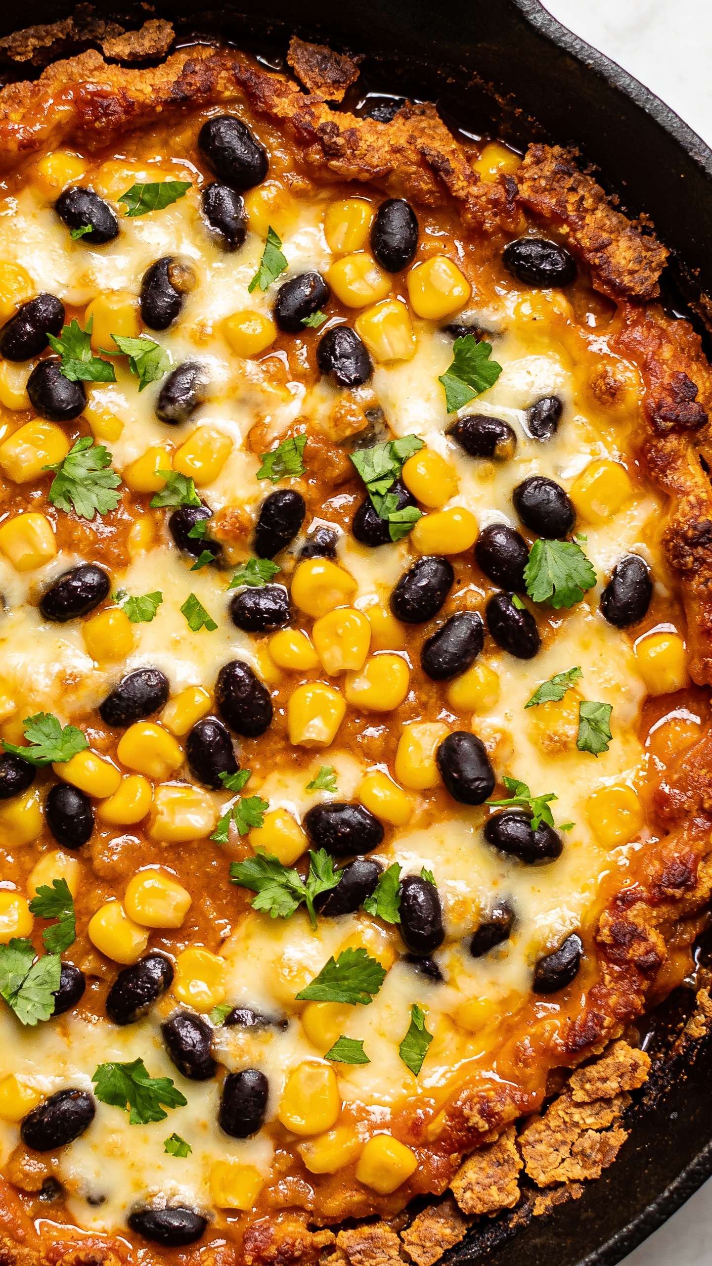 Close-up, top-down angle of the finished casserole focusing on texture: crispy, browned edges around the pan, glossy sauce pooled in the crevices, melted cheese creating a velvety layer, tender corn kernels and black beans visible, cilantro dusting across the surface, bright natural lighting, rich colors, food filling 90–95% of the frame, seamless consistency with the hero image.