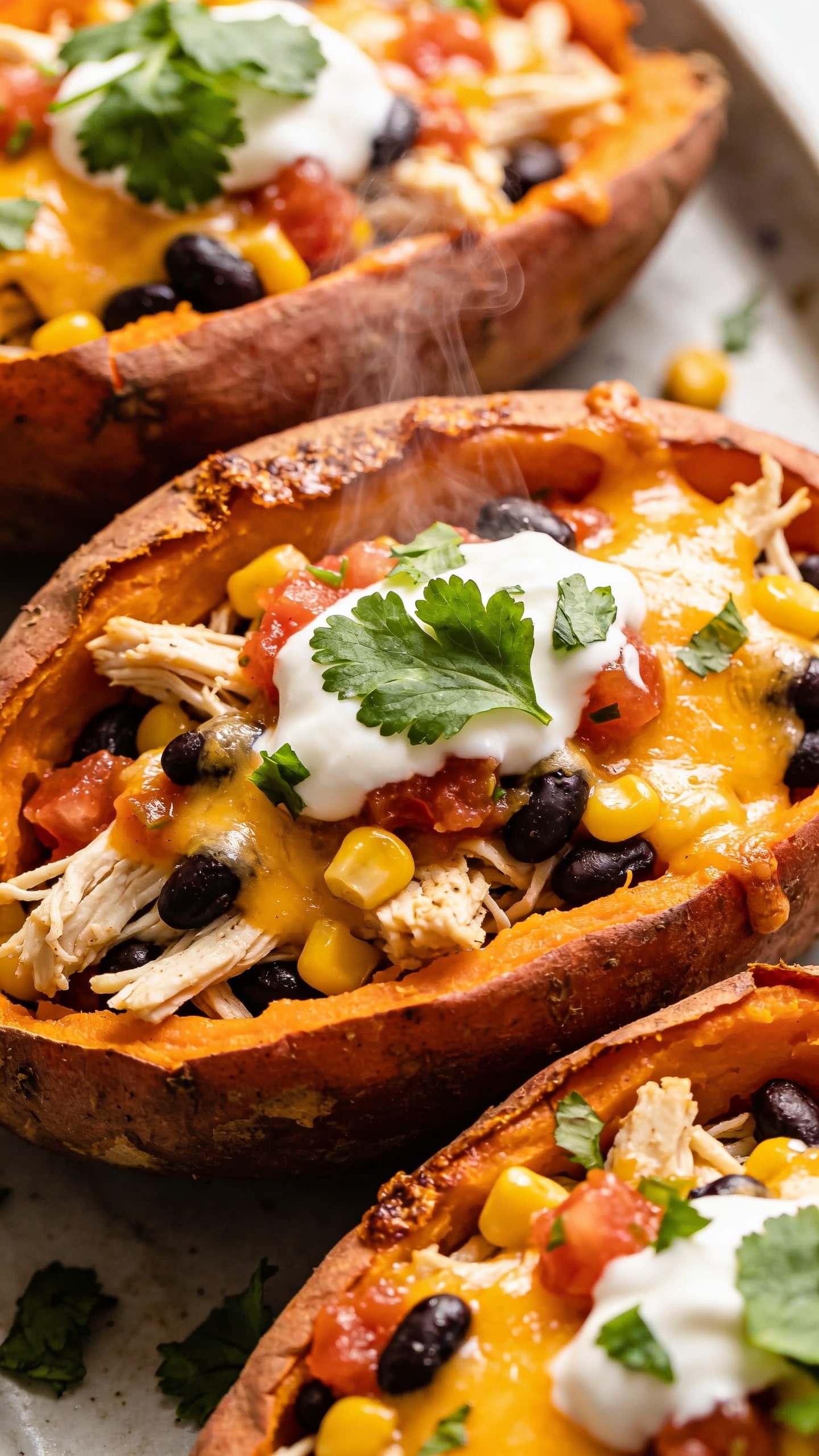 A second ultra-close-up from a different angle (slightly overhead and angled), emphasizing ultra-glossy melted cheese and the savory steam. The shot showcases the stuffed sweet potato halves cut open to reveal shredded chicken, black beans, corn, and salsa, with cilantro leaves and a drizzle of sour cream visible. The lighting is bright and natural, highlighting the textures: crispy potato edges, creamy interior, and rich colors, filling the frame with the finished dish in a premium food-blog style.