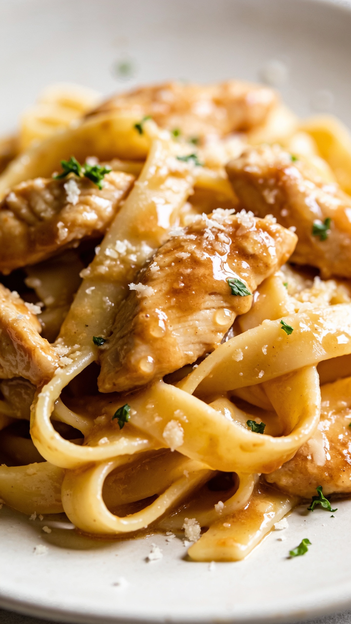 A ultra-close, perspective-forward close-up of the finished pasta from a slightly angled top view, showing juicy chicken, glossy sauce, and melted Parmesan clinging to the pasta, droplets of sauce glistening, a few flecks of fresh parsley sprinkled, bright natural light, shallow depth of field, plate occupying most of the frame to emphasize texture and color.