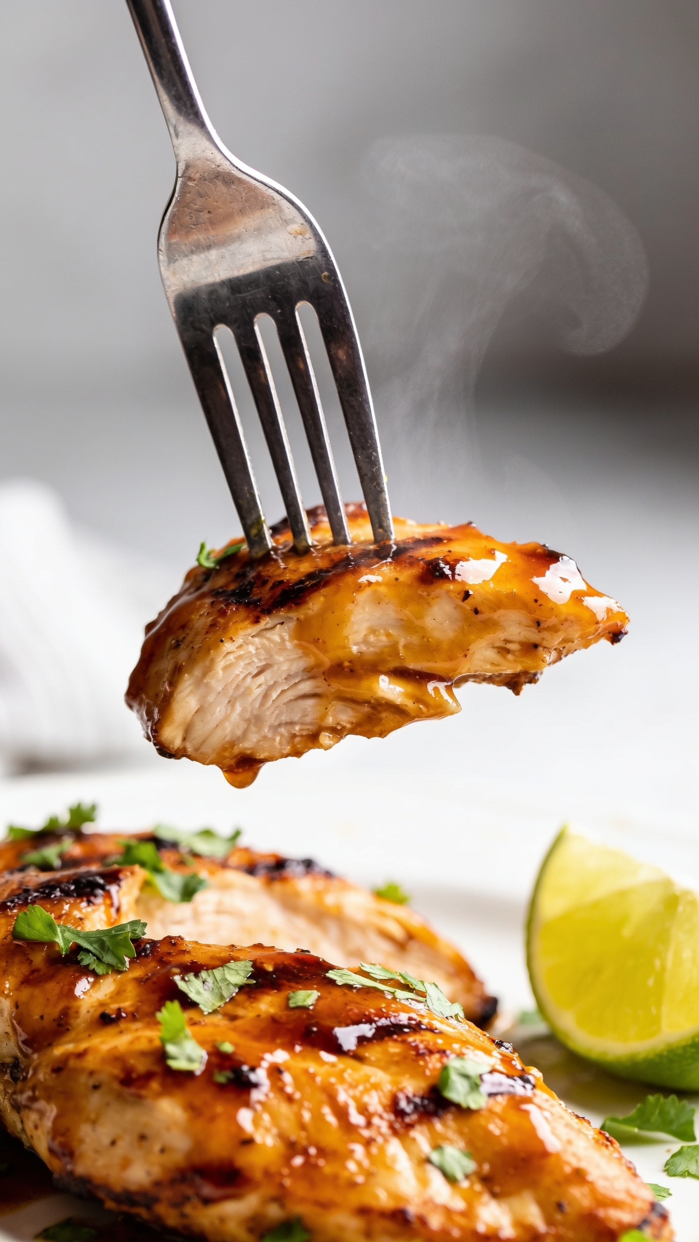 A dynamic close-up action shot capturing the moment just before the perfect bite: a fork tipping to lift a succulent piece of grilled chicken with melted coating, sauce shimmering, steam faintly rising, cilantro flakes and a squeeze of lime in the frame, 90â95% food fill, bright natural lighting, shallow depth of field, no hands or people visible.