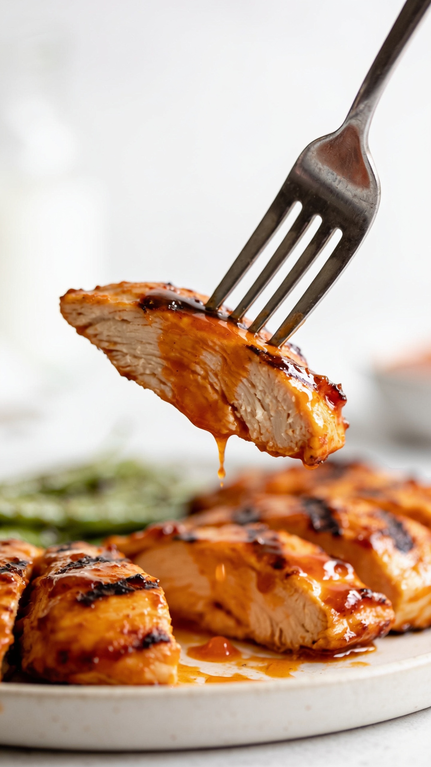 A dynamic close-up action shot: a fork lifting a perfect bite of buffalo-glazed grilled chicken, glaze dripping slightly, juicy interior visible, crisp edges catching the light, glossy sauce catching reflections, premium food-blog styling with a blurred background, 90-95% food fill, bright natural lighting, shallow depth of field, no people.